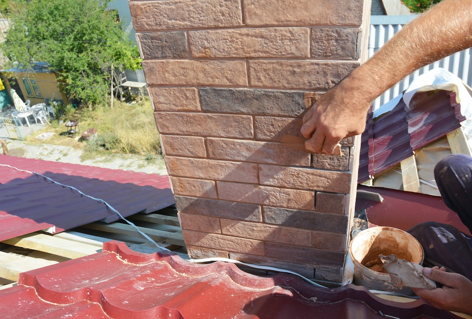 Roofer repair chimney pipe, smoke stake on unfinished house metal roofing construction; roof inspection