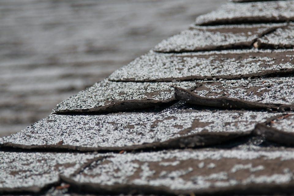 close up view of damaged roof shingles that are curling because of age to tell us how old is my roof