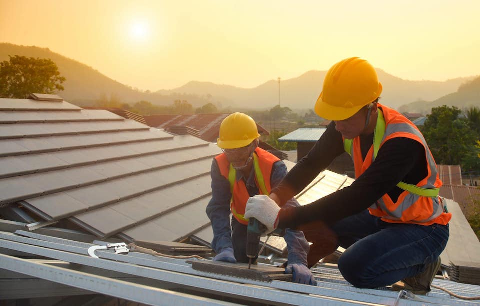 two professional workers installing new roof on home with sunset in the background; DIY roof replacement