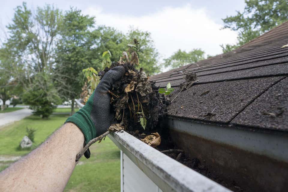 mans arm cleaning out debris from roof gutter; 8 valuable roof maintenance tips