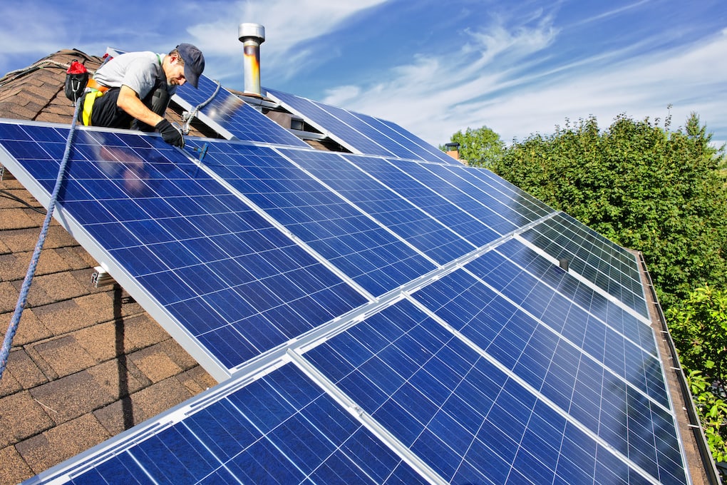 Man installing alternative energy photovoltaic blue solar panel colors on roof