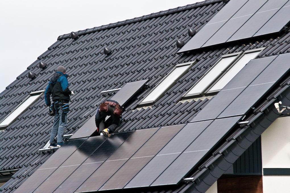 black solar panels on a black metal roof with roof workers installing