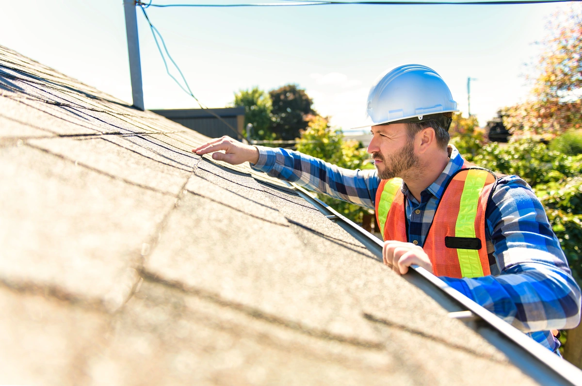 roof tech inspecting a roof while standing on a ladder